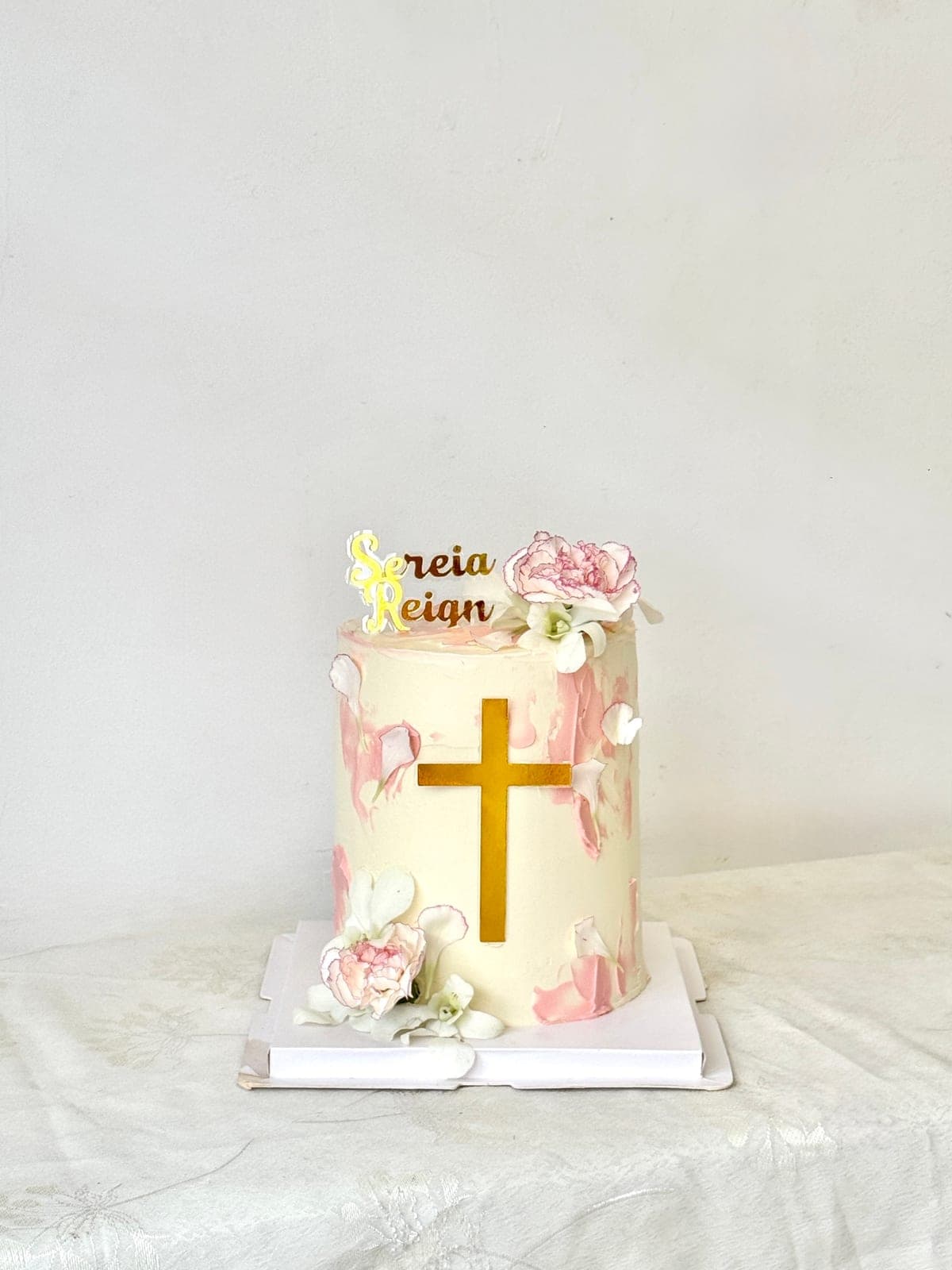Tall christening cake with a gold cross, pink brushstrokes and carnations