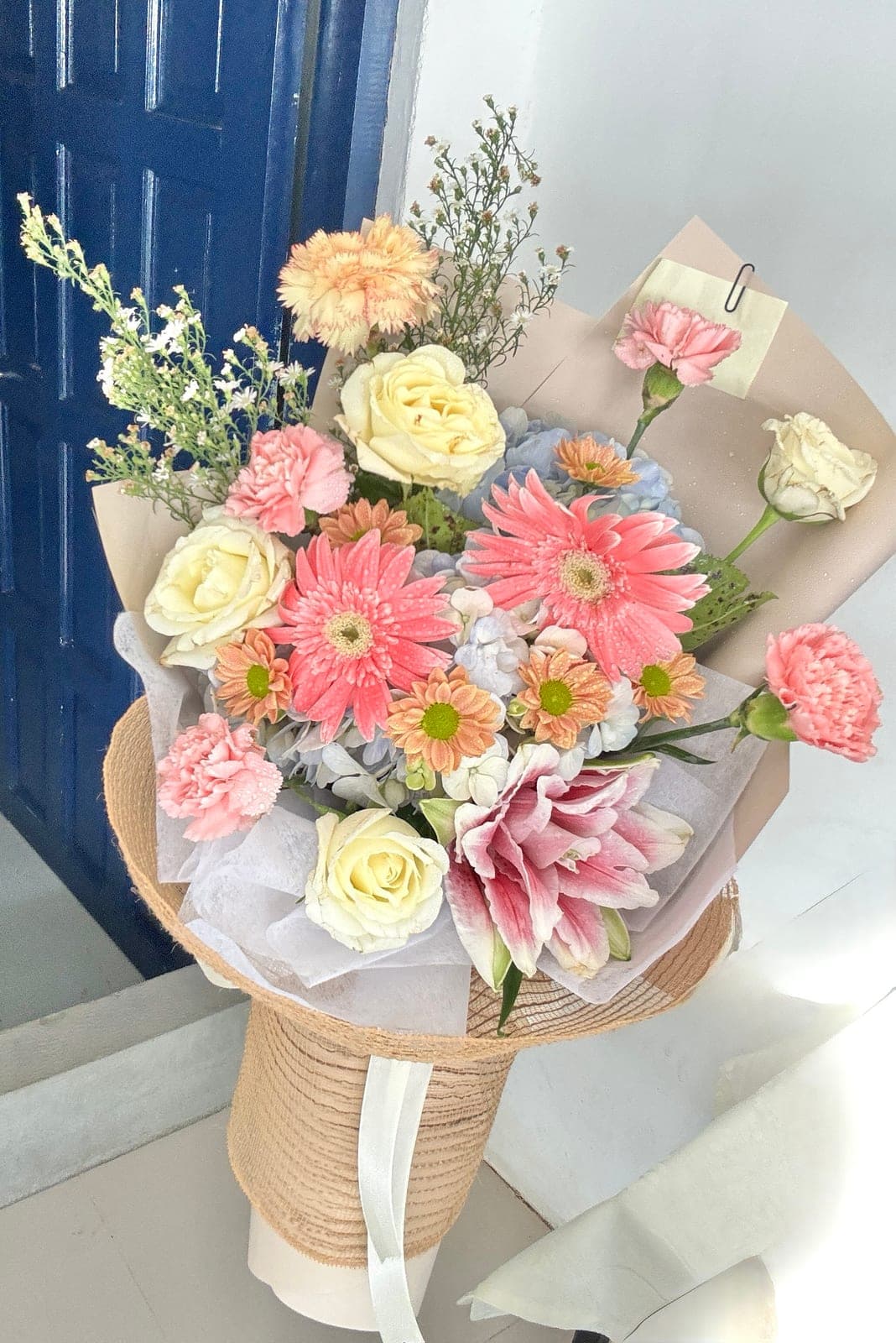 Pastel bouquet of gerberas, roses, carnations and a lily in burlap wrap